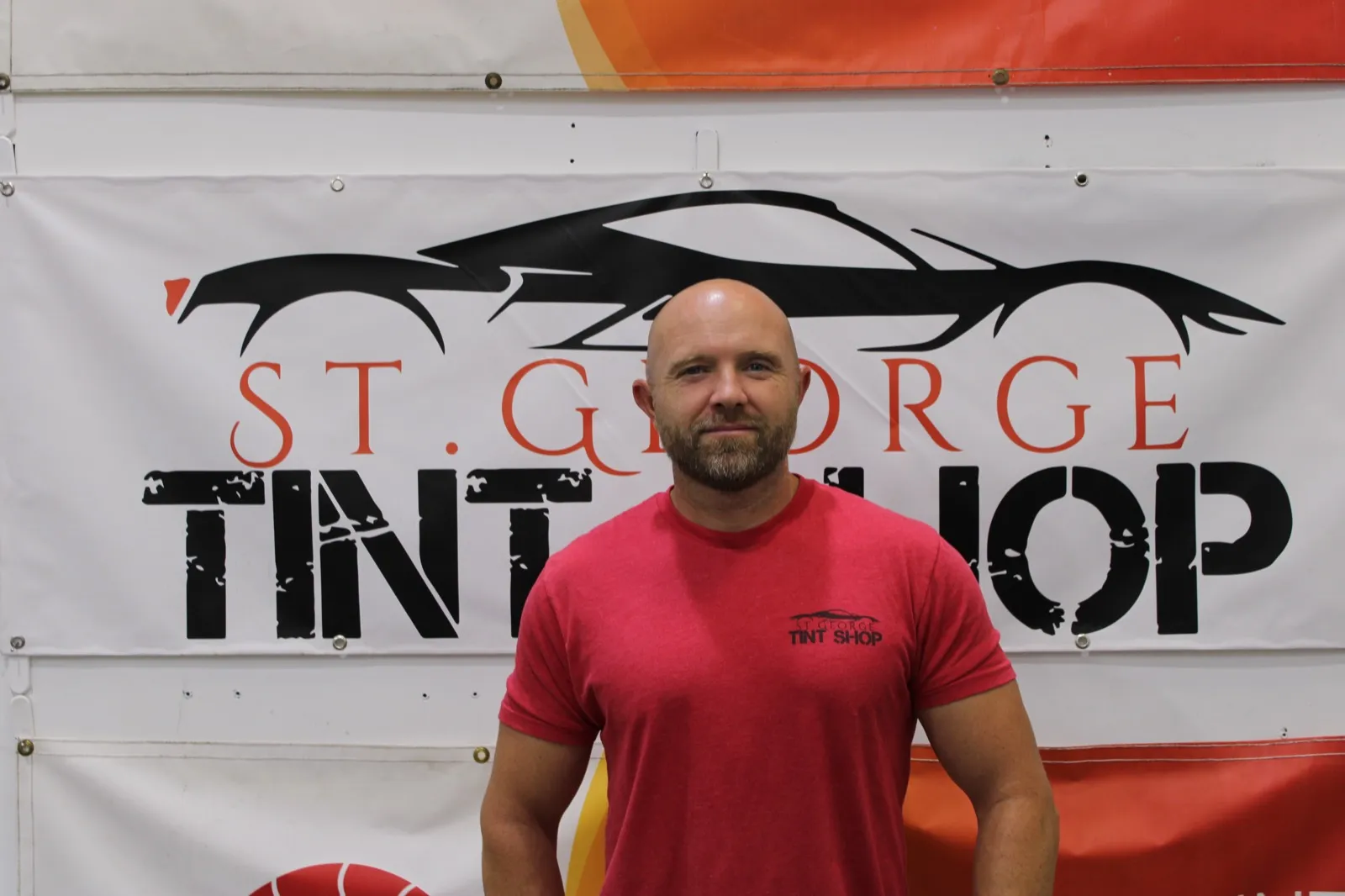 Skyler Householder, owner of St George Tint Shop, standing in front of the shop banner